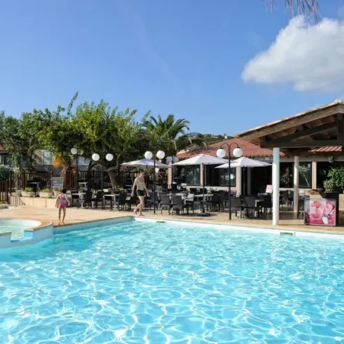 Piscine du camping La Trinité avec parasols et tables autour, sous un ciel bleu.