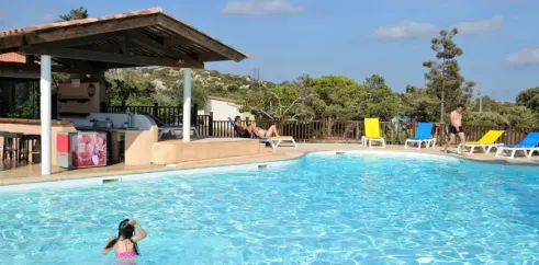 Une enfant nage dans la piscine du Camping La Trinité, avec un bar en bois et des chaises longues colorées.