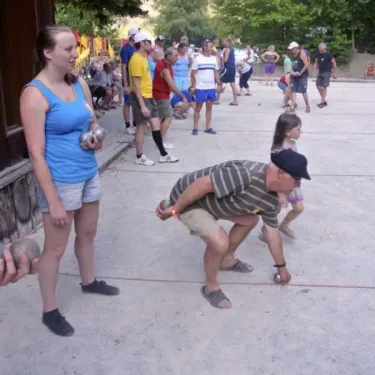 Camping Le Colporteur : jeu de boules dans une cour ensoleillée avec des adultes et enfants.