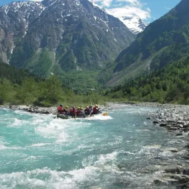Groupes de personnes en rafting dans une rivière en montagne, entourées de pics enneigés.