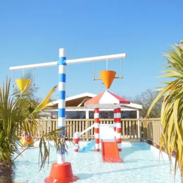 Piscine avec jeux aquatiques et palmiers au Camping La Baie Dorée