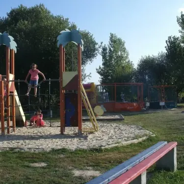 Parc infantile avec toboggans et structures en bois, enfants jouent sur le sable et les arbres entourent l'espace.