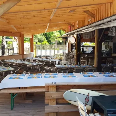 Terrasse du Camping Des Familles avec tables et chaises sous une pergola en bois.