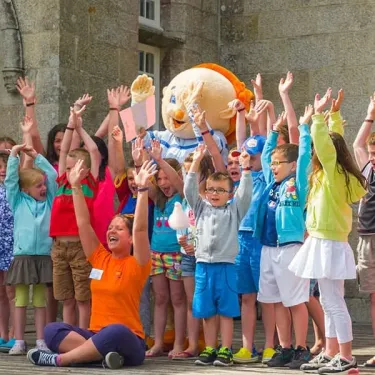 Enfants saluant un mascotte dans une cour du Camping L'Océan Breton