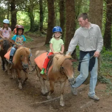 Adulte guide des enfants à cheval sur des poneys dans la forêt à Camping L'Océan Breton.