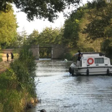 Bateau flottant sur un canal avec des cyclistes sur le chemin adjacent.