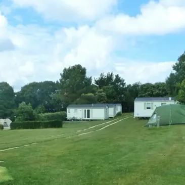 Camping Pré de la Mer : rangées de mobile homes et tente sur pelouse verte.