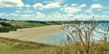 Plage de sable fin avec vue sur l'océan sous un ciel bleu parsemé de nuages