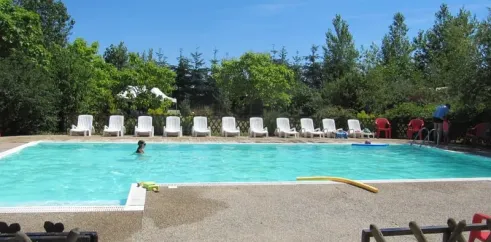 Piscine avec chaises longues et enfant nageant au Camping Ferme de Prunay