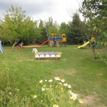 Parc d'attractions pour enfants avec toboggan, balançoire et cheval mécanique dans le jardin du camping Camping Ferme de Prunay