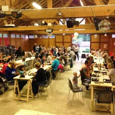 Camping La Plage de Garoustel : salle de repas en bois avec des tables et chaises, des personnes dégustant un repas.