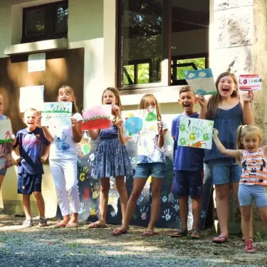 Camping La Plage de Garoustel : enfants souriants tenant leurs œuvres d'art sur le terrain extérieur.