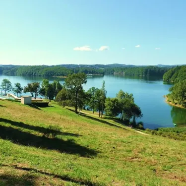 Lac avec bordure verdoyante et cabanes au Camping La Plage de Garoustel