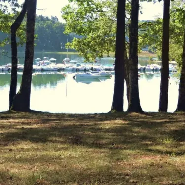 Camping La Plage de Garoustel : vue par les arbres sur un lac avec des bateaux