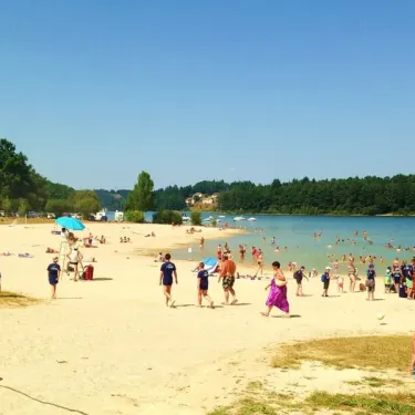 Camping La Plage de Garoustel : plage animée avec enfants et adultes, près d’un lac, sous un ciel bleu.