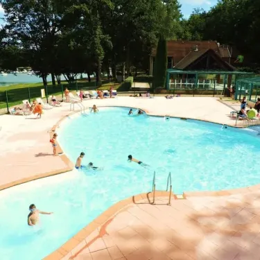 Piscine entourée de chaises longues près d'un lac au Camping La Plage de Garoustel