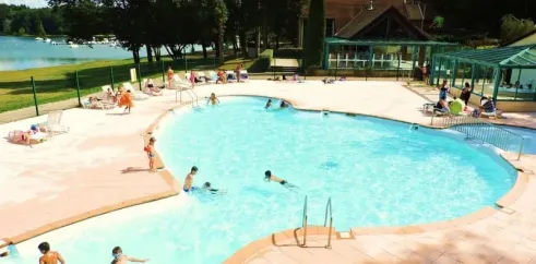 Piscine entourée de chaises longues près d'un lac au Camping La Plage de Garoustel