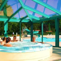 Camping La Plage de Garoustel : groupe dans une baignoire à remous sous un toit en verre avec piscine et toboggan en arrière-plan.