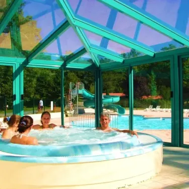 Camping La Plage de Garoustel : groupe dans une baignoire à remous sous un toit en verre avec piscine et toboggan en arrière-plan.