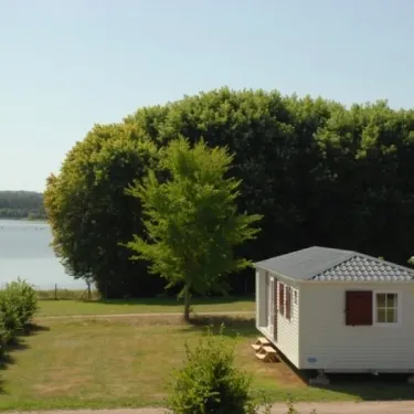 Mobile home blanc près d'un lac, entouré de verdure, au Camping Des Lacs.