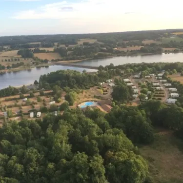 Vue aérienne du camping avec des mobile homes, une piscine et un lac environnant.