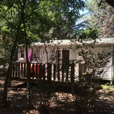 Cabane de camping blanc entourée d'arbres, avec balcon en bois et vêtements suspendus à sécher.