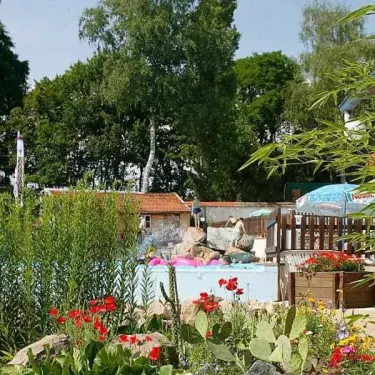 Piscine entourée de plantes et fleurs dans le jardin du Camping Le Manoir de Bezolle