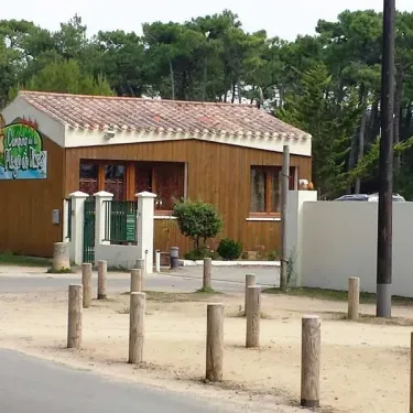 Entrée du Camping La Plage de Riez avec une maison en bois, portail vert et poteaux en bois devant un parcours forestier.