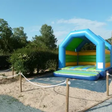 Bouncer gonflable bleu et vert au Camping Les Samaras, entouré d'une clôture en bois.
