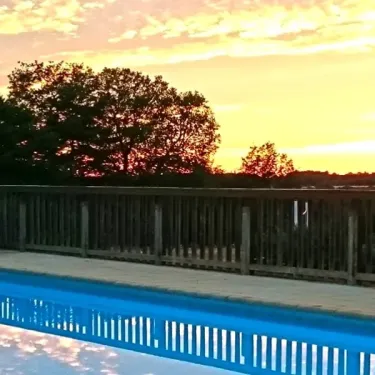 Coucher de soleil sur une piscine entourée d'une balustrade en bois à Camping La Nouvelle Croze