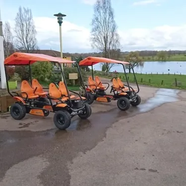 Trois véhicules électriques orange stationnés près d'un lac. Camping Des Lacs.