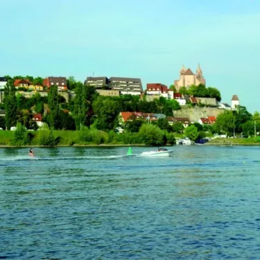 Camping L'Ile du Rhin : rivière avec bateau et personne en planche à voile, ville sur une colline au loin