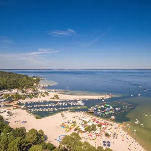 Vue aérienne du Camping Slow Village : plage, marina, jeux aquatiques et forêt environnante.