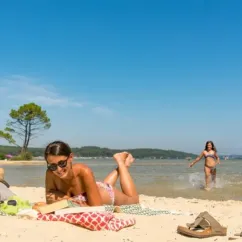 Femme lisant sur une plage avec enfants qui jouent dans l'eau au Camping Slow Village