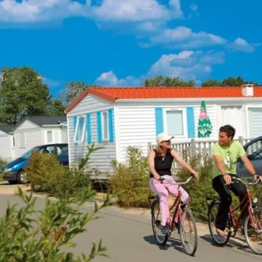 Un couple à vélo devant des mobil-homes au Camping L'Etang de Besse, sous un ciel bleu.