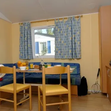 Intérieur du camping Kerarno : canapé-lit, table, chaises en bois et téléviseur.