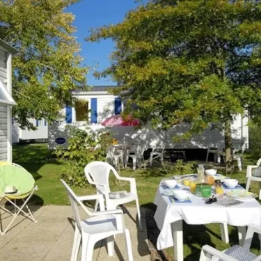 Camping Kerarno : table à l'extérieur avec chaises blanches et cabane en bois.