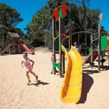 Enfant qui court sur le sable près d'un toboggan jaune au Camping Les Demoiselles
