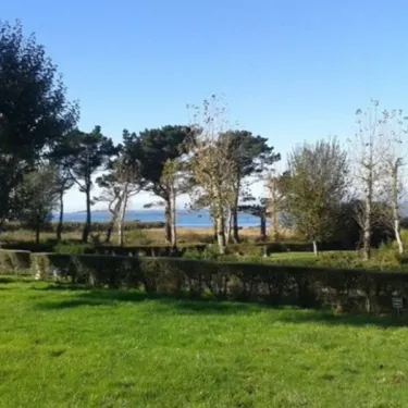 Camping Port de la Chaine : vue panoramique sur la mer depuis un parc verdoyant avec haies et arbres.