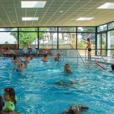 Groupes d'enfants et d'adultes nageant joyeusement dans la piscine intérieure du Camping Port de la Chaine