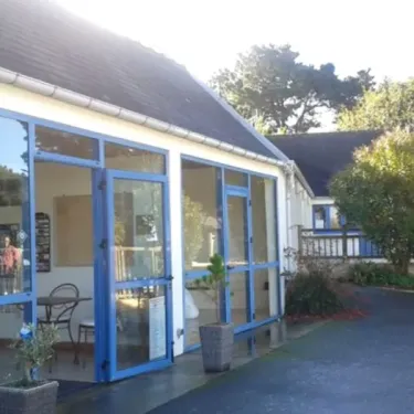 Camping Port de la Chaine : bâtiment avec grandes fenêtres bleues, terrasse extérieure et jardin fleuri.