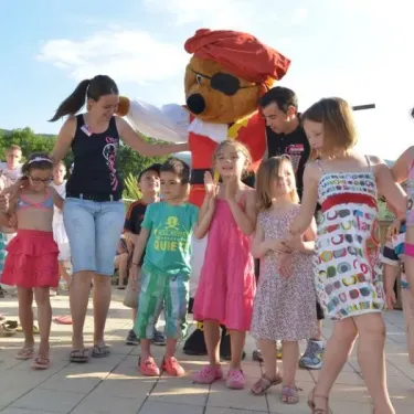 Personnages costumés et enfants en maillots de bain sur une terrasse ensoleillée. Camping Les Albères.
