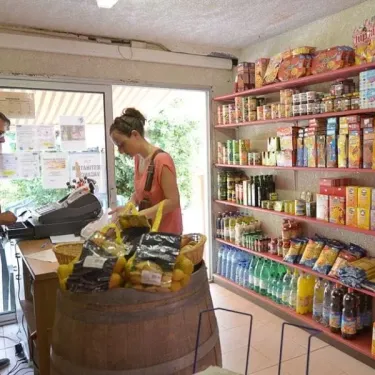 Magasin de camping Camping Les Albères avec des étagères remplies de produits et un comptoir en bois.