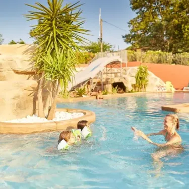 Enfants dans une piscine avec toboggan intégré, entourés de rochers décoratifs. Camping Les Albères.