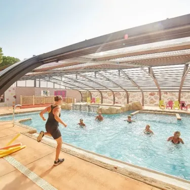 Piscine couverte avec des enfants nageant et un adulte courant près du bord. Camping Les Albères.