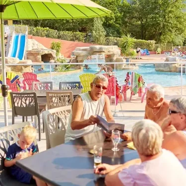 Groupe âgé dégustant un repas sous une ombrelle près d'une piscine à Camping Les Albères.