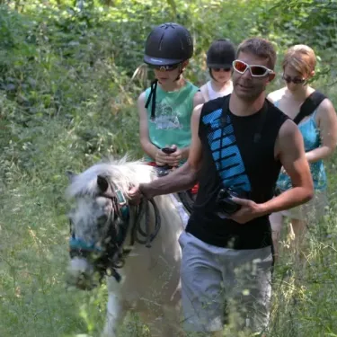 Adulte guide un poney dans une forêt verte à Camping Les Albères.