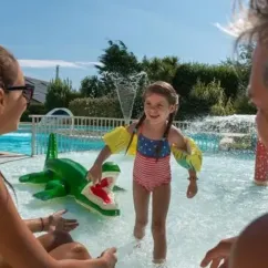 Une petite fille joue avec un dauphin gonflable dans la piscine du camping Les Iles.