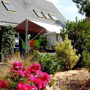 Camping Les Iles : maison avec toit en ardoise et fleurs roses en avant-plan