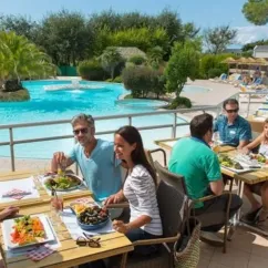 Des visiteurs dégustent un repas en plein air près de la piscine du camping Les Iles.
